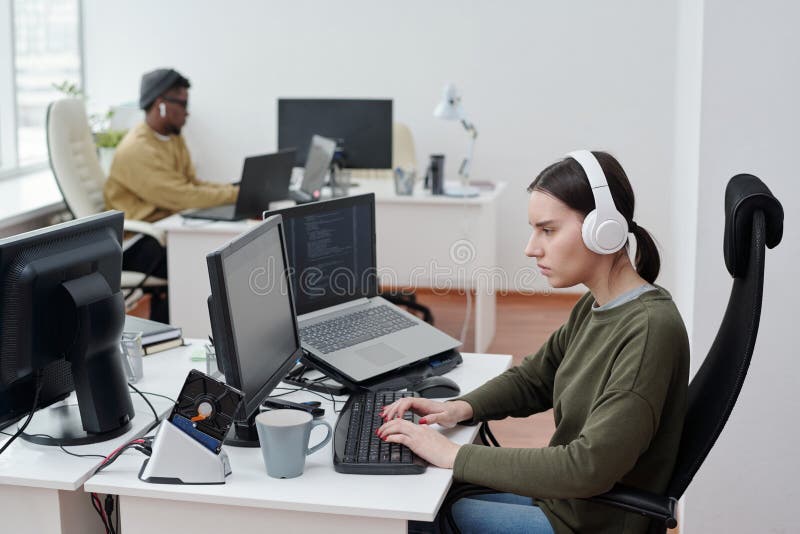 Side view of female programmer in headphones listening to music by workplace stock image