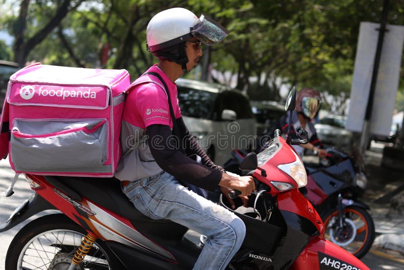 A close-up of a Foodpanda rider near a road junction in Ipoh Malaysia. The big food container bag is sling to the rider's back. A close-up of a Foodpanda rider near a road junction in Ipoh Malaysia. The big food container bag is sling to the rider's back