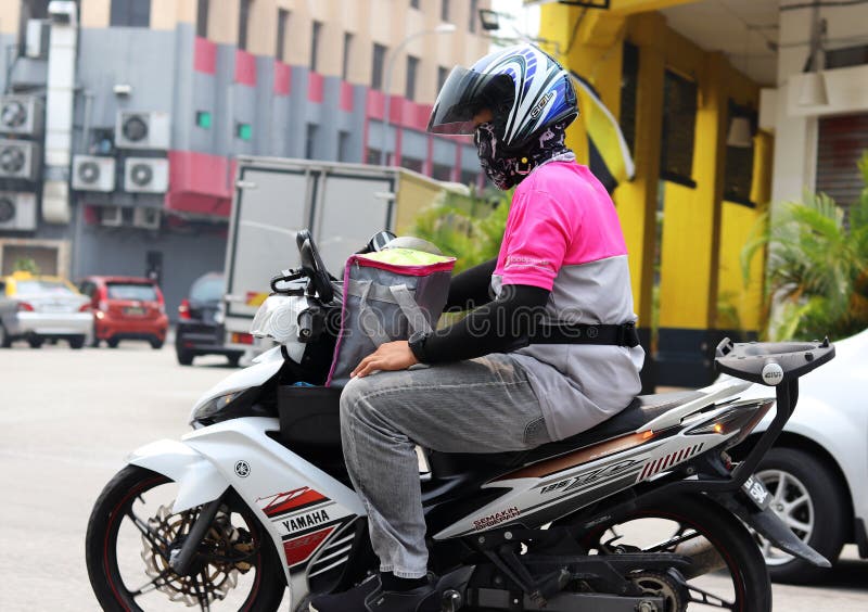 Foodpanda rider in Ipoh Malaysia wearing a face mask to filter out air pollutants in the city. The food container bag is place in the front motorcycle carrier basket instead of the back. Foodpanda rider in Ipoh Malaysia wearing a face mask to filter out air pollutants in the city. The food container bag is place in the front motorcycle carrier basket instead of the back