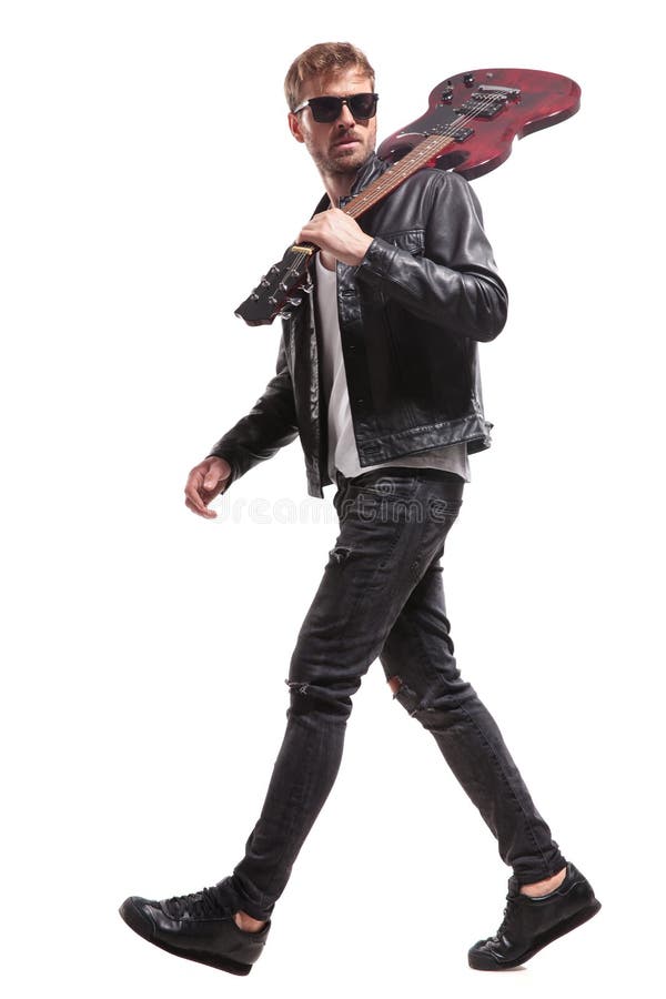 Side view of handsome rocker walking with guitar on shoulder