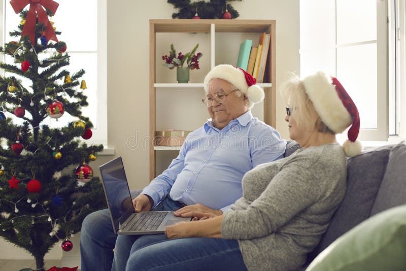 Side view of happy senior couple using laptop watching favorite Christmas movies. Christmas mood. Side view of happy senior couple using laptop watching stock photo