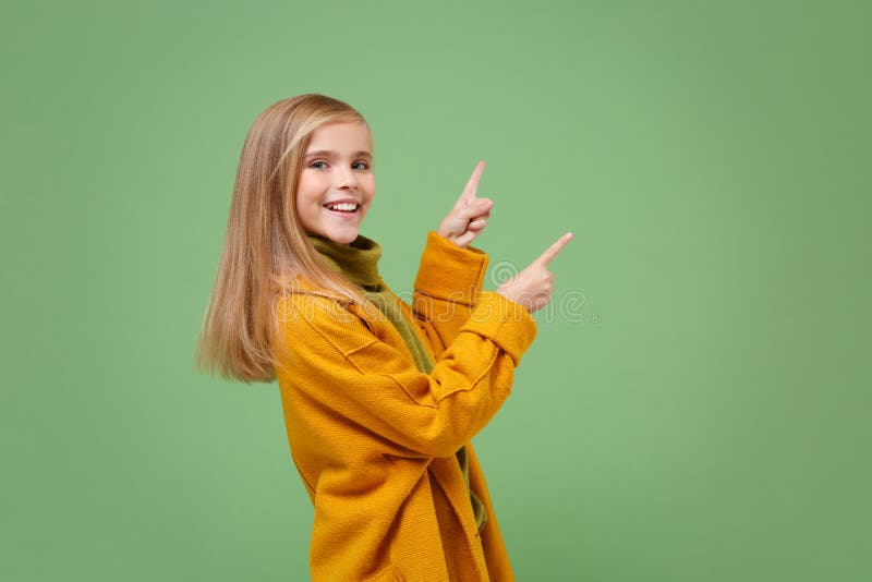 Side view of little blonde kid girl 12-13 years old in yellow coat posing isolated on pastel green background in studio