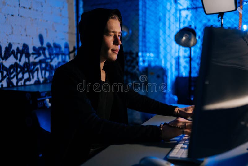 Side view of male hacker wearing hoods hacking to steal important information using computer to release malware viruses Ransom and harass organizations, in dark basement room with blue neon lights.