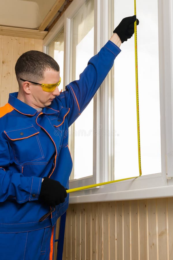 Side view of a man in  construction clothing measuring a window opening with a tape measure