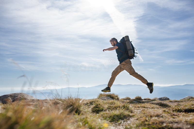 Mature man with backpack hiking in mountains in summer, jumping.