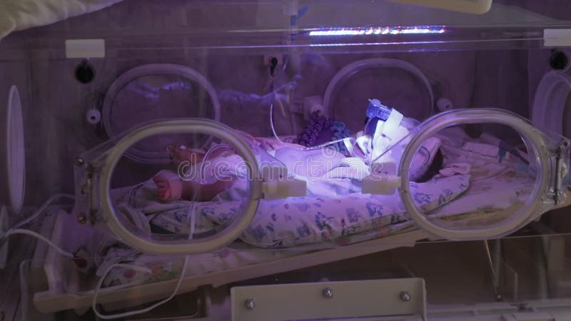 Side view of newborn baby lying inside a crib at a hospital. Baby in incubator under the supervision of doctors. Intensive care unit