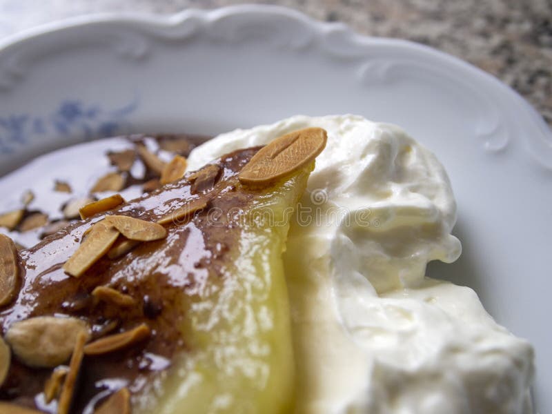 Side view of one poached caramelized pear with whipped cream, chocolate sauce and almond flakes