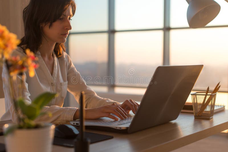Side view photo of a female programmer using laptop, working, typing, surfing the internet at workplace. stock images