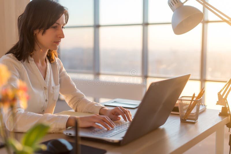 Side view photo of a female programmer using laptop, working, typing, surfing the internet at workplace. stock image