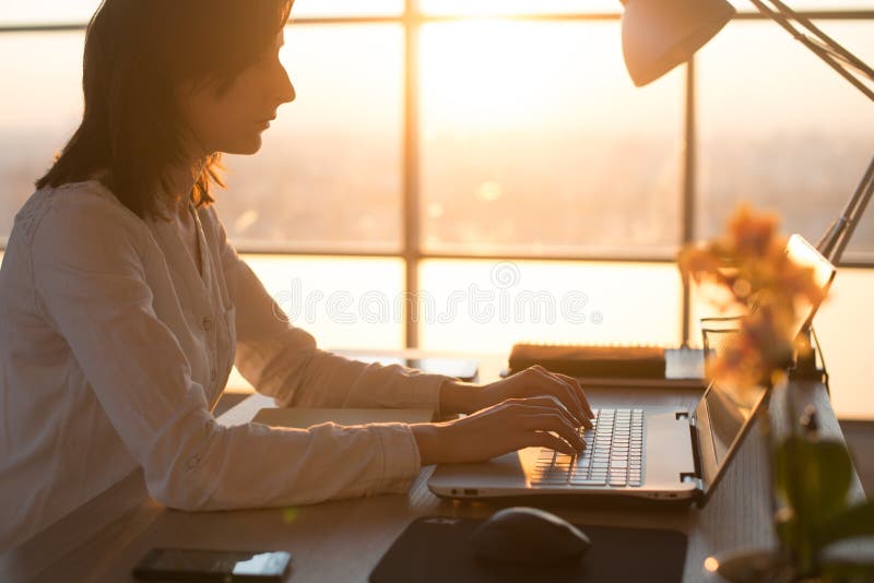 Side view photo of a female programmer using laptop, working, typing, surfing the internet at workplace. stock images