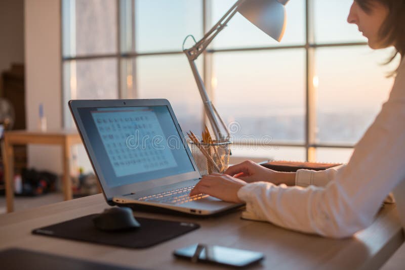 Side view photo of a female programmer using laptop, working, typing, surfing the internet at workplace. stock photography