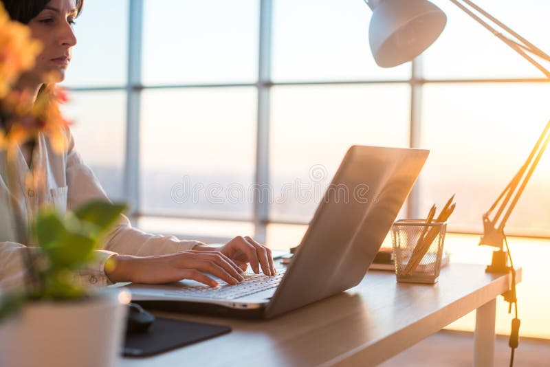 Side view photo of a female programmer using laptop, working, typing, surfing the internet at workplace. stock image