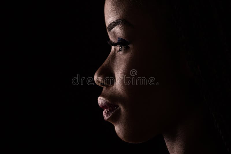 Side view portrait of dark skinned model on a black background.