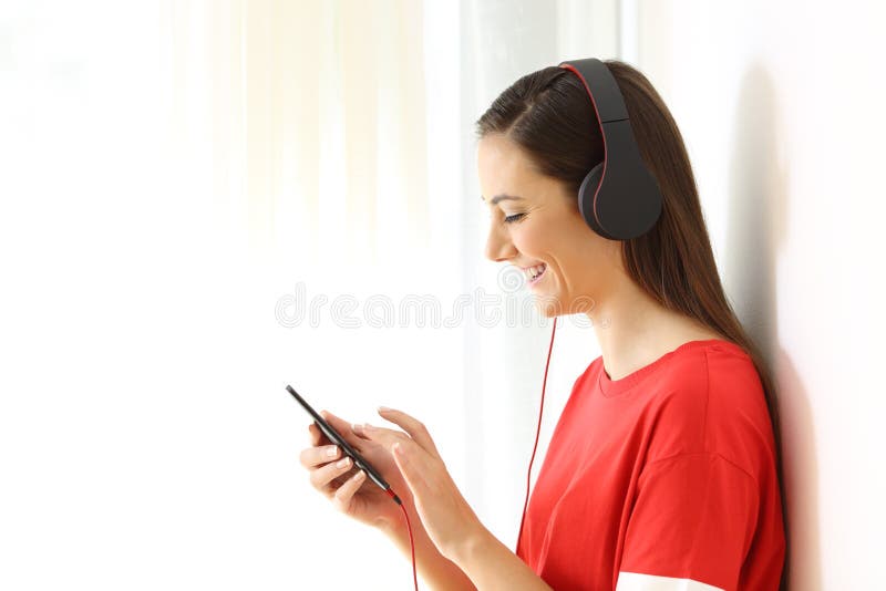 Side view portrait of a girl listening to music on line with a smart phone and headphones isolated on white at side. Side view portrait of a girl listening to music on line with a smart phone and headphones isolated on white at side