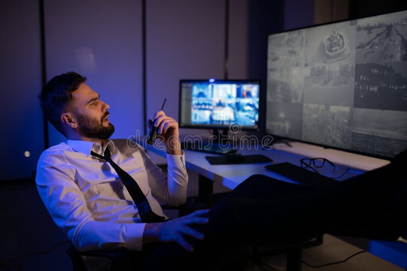 Side view of security system operator using walkie talkie while looking at CCTV footage stock photos