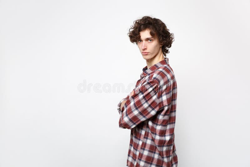 Side view of serious young man in casual clothes looking camera and holding hands crossed isolated on white wall stock image