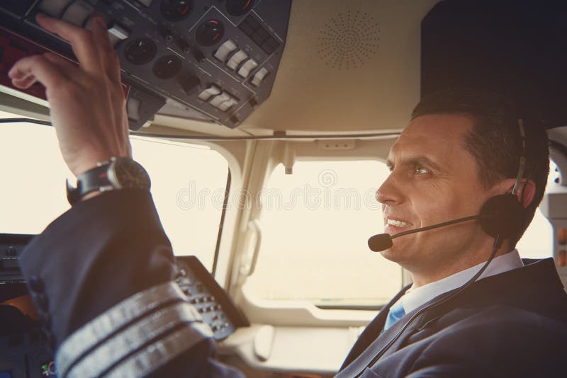 Cheerful aviator pressing buttons in cockpit royalty free stock photo