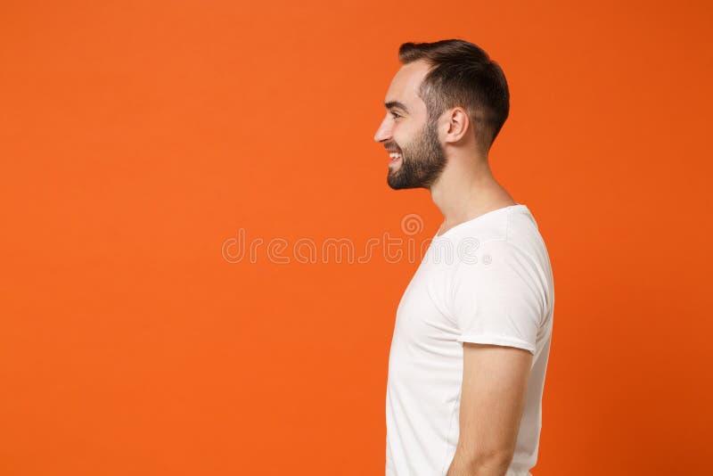 Side view of smiling young man in casual white t-shirt posing isolated on bright orange wall background, studio portrait stock image