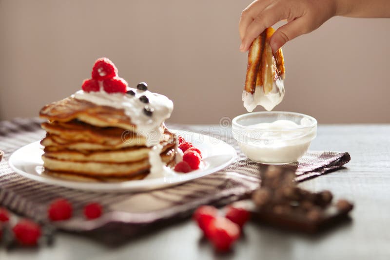 Side view of traditional family pancakes with sour cream and fresh berries on dark background, woman`s hand dipping royalty free stock image Side view of traditional family pancakes with sour cream and fresh berries on dark background, woman`s hand dipping royalty free stock image