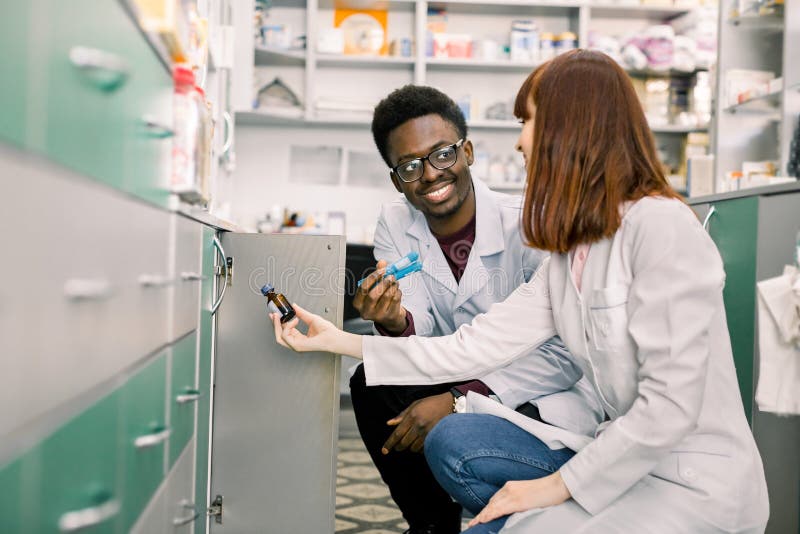 Side view of two dedicated pharmacists, African men and Caucasian woman, looking for the best medicine while working together in a community pharmacy. Side view of two dedicated pharmacists, African men and Caucasian woman, looking for the best medicine while working together in a community pharmacy.