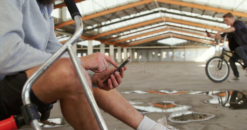 BMX riders using smartphones in an empty warehouse