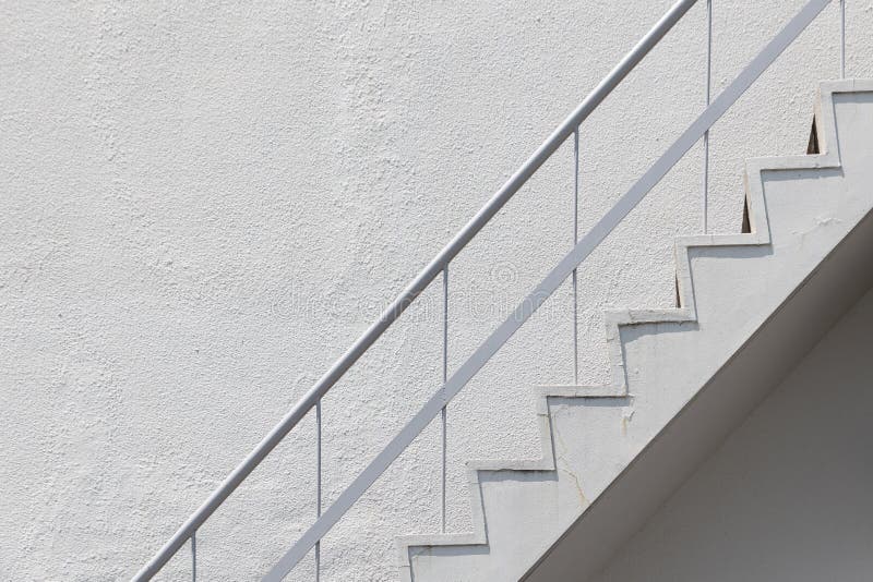 Side view of white outside fire escape emergency staircase with metal handrail railing and concrete wall stock image Side view of white outside fire escape emergency staircase with metal handrail railing and concrete wall stock image