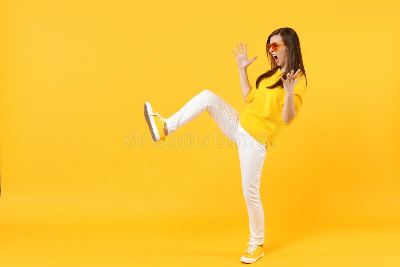 Side view of wild young woman in casual clothes, heart glasses showing palms kicking something  on yellow orange royalty free stock photography
