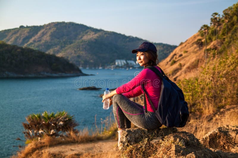 Side view of woman with backpack and a bottle of water looking at sea while sitting on hill against sky . royalty free stock images Side view of woman with backpack and a bottle of water looking at sea while sitting on hill against sky . royalty free stock images