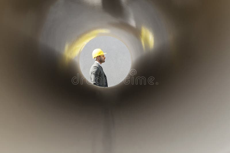Side view of young male architect through large pipe at construction site royalty free stock photos