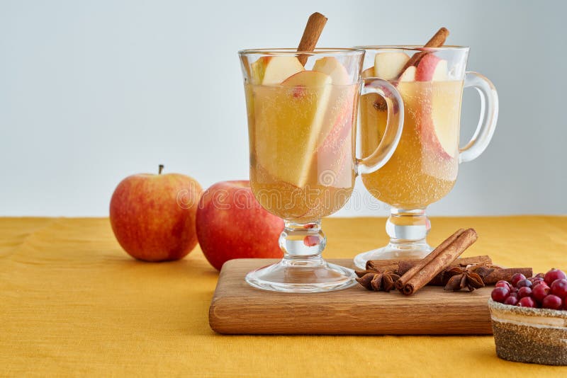 Apple cider. Two glasses of hot white mulled wine beverages with cardamom, cinnamon on wooden board on linen tablecloth. Apple toddy. Seasonal winter beverage. Selective focus, blurred background. Apple cider. Two glasses of hot white mulled wine beverages with cardamom, cinnamon on wooden board on linen tablecloth. Apple toddy. Seasonal winter beverage. Selective focus, blurred background