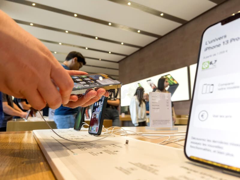 Paris, France - Sep 9, 2022: Side view of woman hands holding latest iPhone 13 Pro telephone with customers in background shopping for gifts for the upcoming winter holiday. Paris, France - Sep 9, 2022: Side view of woman hands holding latest iPhone 13 Pro telephone with customers in background shopping for gifts for the upcoming winter holiday