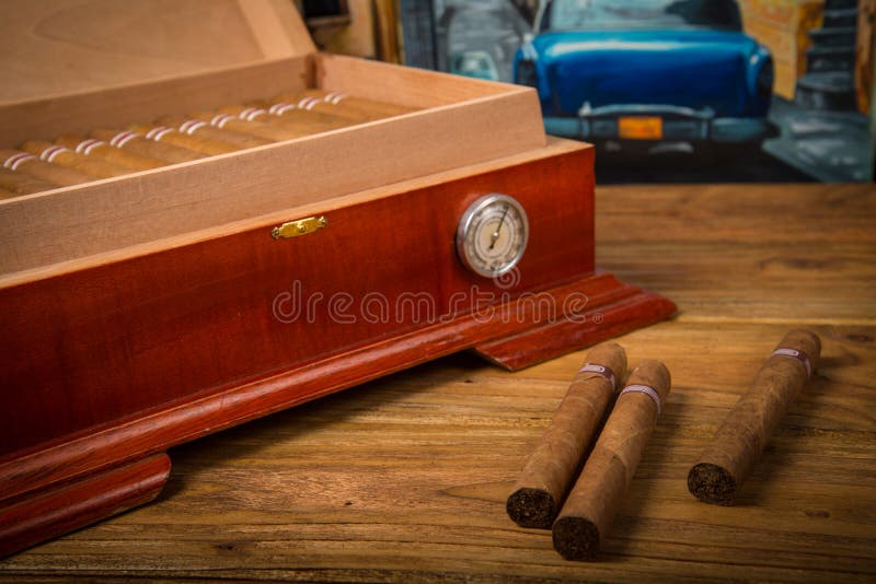 Cuban cigars and humidor on rustic wooden table with Cuban painting of american old car in background. Cuban cigars and humidor on rustic wooden table with Cuban painting of american old car in background
