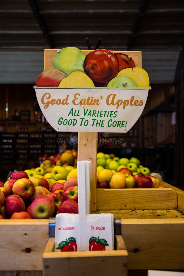 A sign near wooden containers filled with apples under the lights with a blurry background