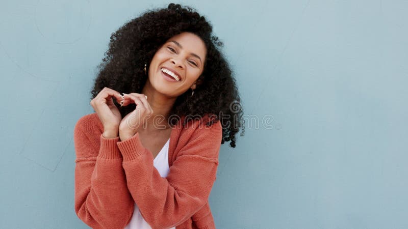 Signe d'amour sourire et femme noire heureuse debout isolée sur un fond de studio bleu maquette. romance de fille et main