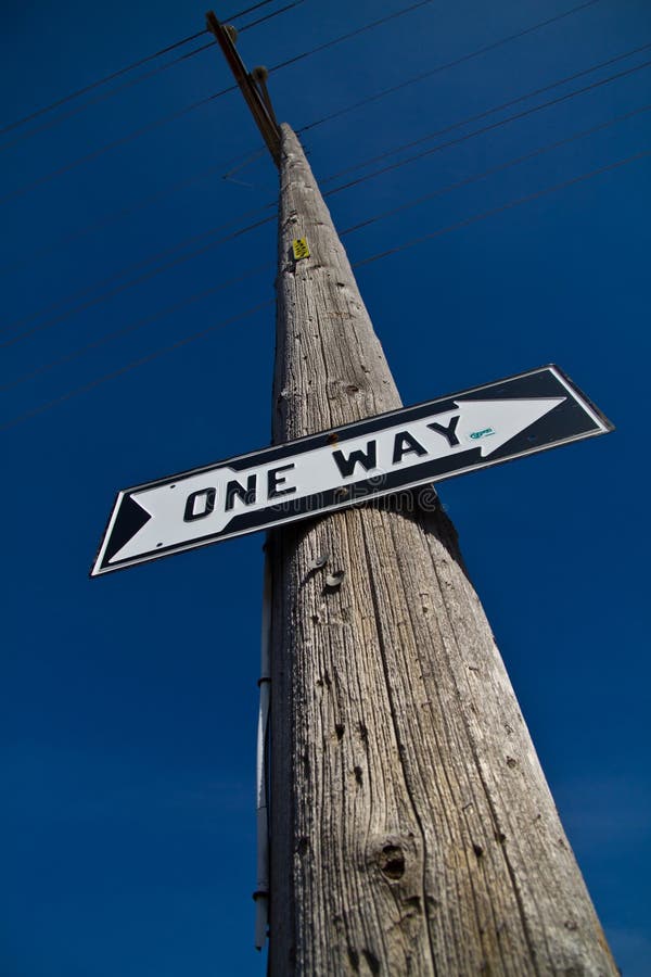 Clear Direction: A weathered utility pole in Allegan, Michigan proudly displays a &#x27;ONE WAY&#x27; sign, pointing left against a vast blue sky, symbolizing certainty, decision-making, and a singular path forward. Clear Direction: A weathered utility pole in Allegan, Michigan proudly displays a &#x27;ONE WAY&#x27; sign, pointing left against a vast blue sky, symbolizing certainty, decision-making, and a singular path forward.