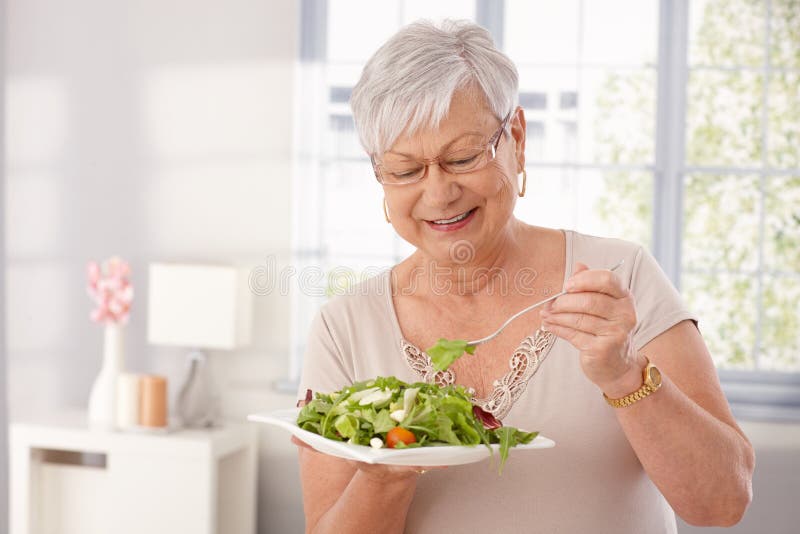 Signora anziana che mangia insalata verde