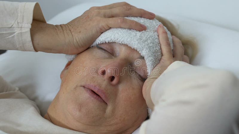 Signora anziana malata che tiene testa con l'asciugamano bagnato sulla fronte, soffrente dalla febbre