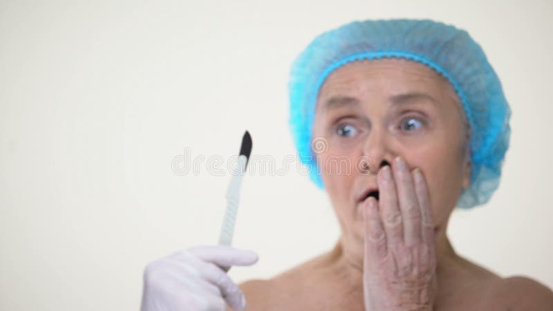 Signora anziana sorridente spaventata del bisturi chirurgico, timore di trattamento, chirurgia plastica