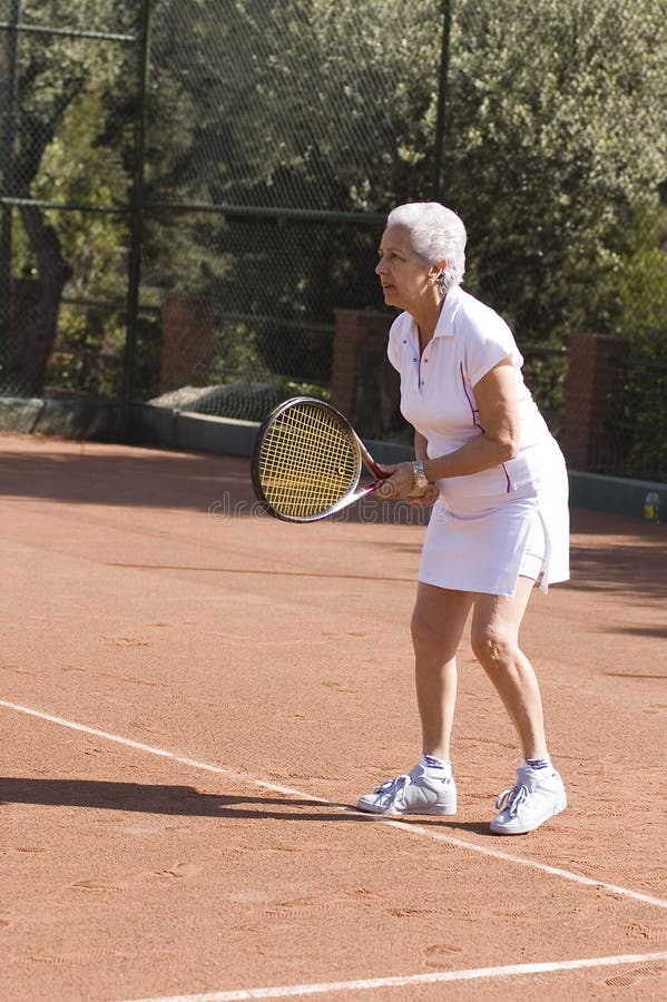 Active attractive senior woman playing tennis in a clay-court. Active attractive senior woman playing tennis in a clay-court