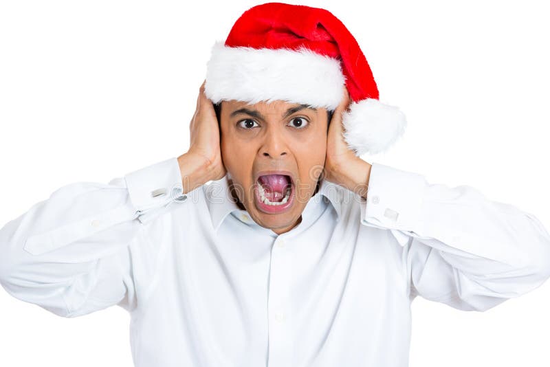 Closeup portrait of mean young man in red santa claus hat covering closing ears with hands to block loud noise, yelling isolated on white background with space to left. Human emotion facial expression. Closeup portrait of mean young man in red santa claus hat covering closing ears with hands to block loud noise, yelling isolated on white background with space to left. Human emotion facial expression