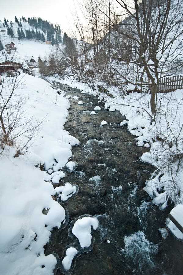 Sikt av djupfryst flodbygd Bäck i snöig landskap Rumänsk liten flod i vinterlandskap, Rumänien, Moeciu Wild bäck royaltyfri foto