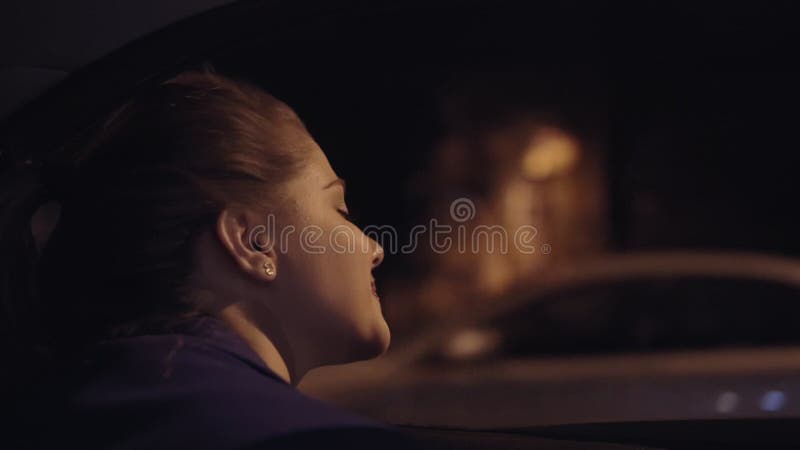 Sikt från bilen: härlig ung kvinna som lutar ut från bilfönstret och ser staden på natten Slowmotion
