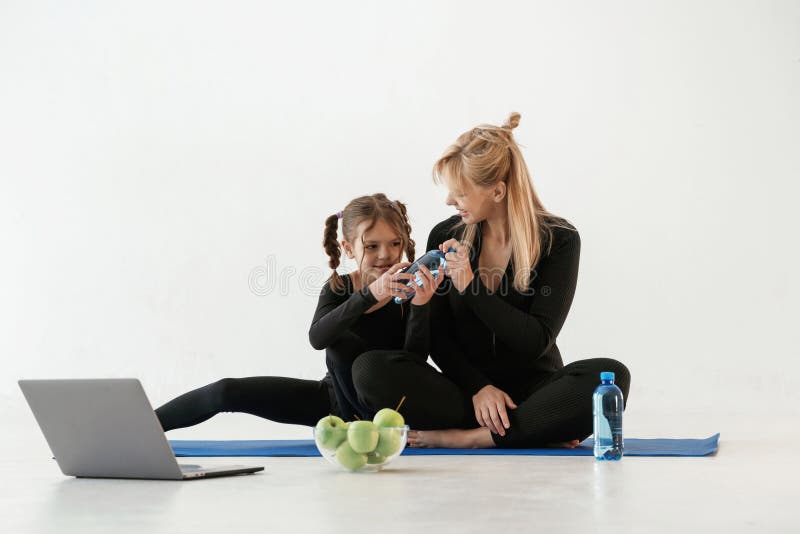 Silberfarbene Laptop-Äpfel und Wasser. Mutter und kleine Tochter sind auf Yogamat in Fitnesskleidung lizenzfreie stockfotos