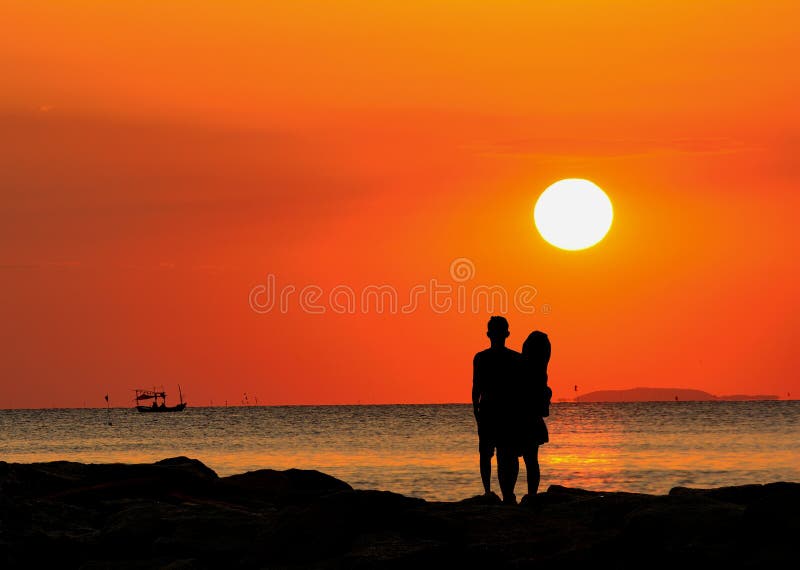 Silhouet die van paar zich door het overzees bevinden die op de zonsondergang letten stock afbeeldingen Silhouet die van paar zich door het overzees bevinden die op de zonsondergang letten stock afbeeldingen