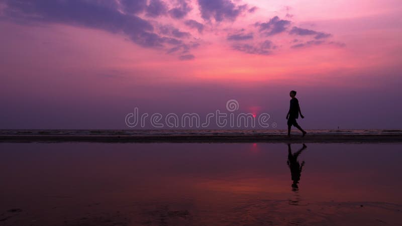 Silhouet Eenzame Aziatische jonge mens die vreedzaam langs een verlaten strand bij zonsondergang lopen Zeegezicht stock foto Silhouet Eenzame Aziatische jonge mens die vreedzaam langs een verlaten strand bij zonsondergang lopen Zeegezicht stock foto