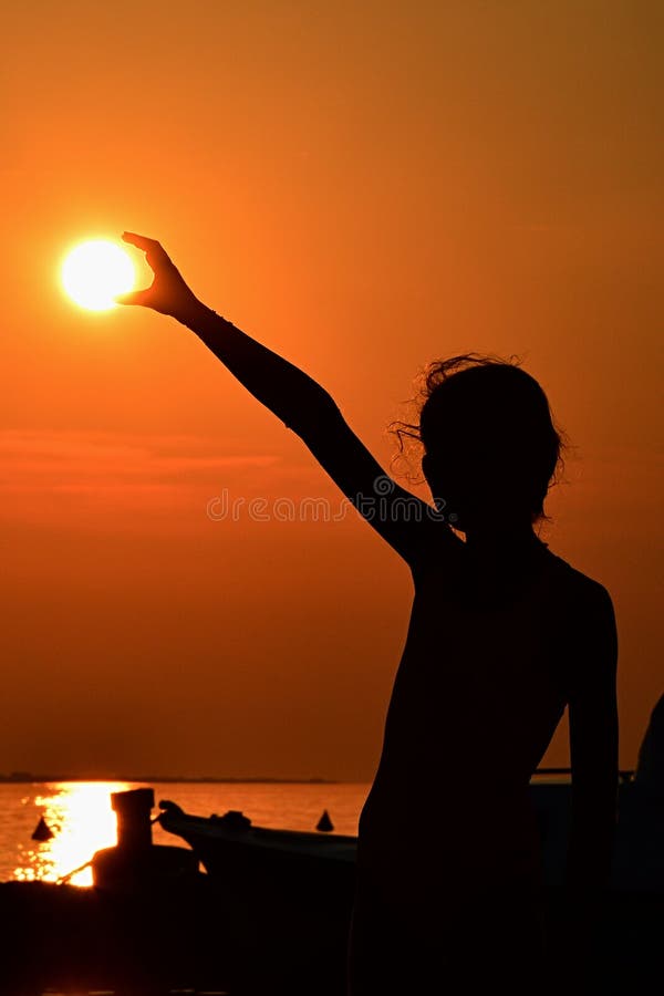 Silhouet van de kleine zon van de meisjesholding tijdens zonsondergang boven jachthaven, deel van motorboot een zichtbaar op rech royalty-vrije stock afbeelding Silhouet van de kleine zon van de meisjesholding tijdens zonsondergang boven jachthaven, deel van motorboot een zichtbaar op rech royalty-vrije stock afbeelding