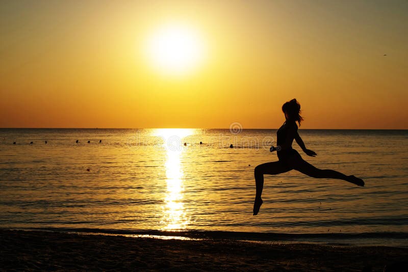 Silhouet van een meisje in een badpak dat langs het strand op de achtergrond van de dageraad loopt royalty-vrije stock afbeelding Silhouet van een meisje in een badpak dat langs het strand op de achtergrond van de dageraad loopt royalty-vrije stock afbeelding