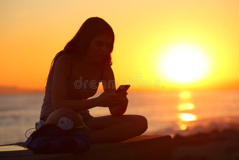 Silhouet van een meisje die een smartphone met behulp van bij zonsondergang royalty-vrije stock afbeelding Silhouet van een meisje die een smartphone met behulp van bij zonsondergang royalty-vrije stock afbeelding