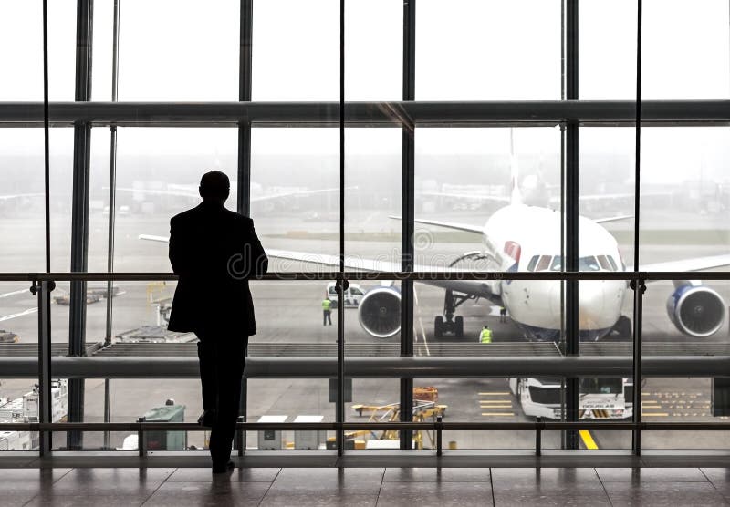 London, UK - August 14, 2015: Silhouette of a traveler waiting for a plane at the Heathrow airport departure hall on a rainy day. London, UK - August 14, 2015: Silhouette of a traveler waiting for a plane at the Heathrow airport departure hall on a rainy day.