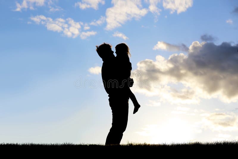 The silhouette of a happy young father holding his little girl child and hugging her as they stand outside at dusk. The silhouette of a happy young father holding his little girl child and hugging her as they stand outside at dusk